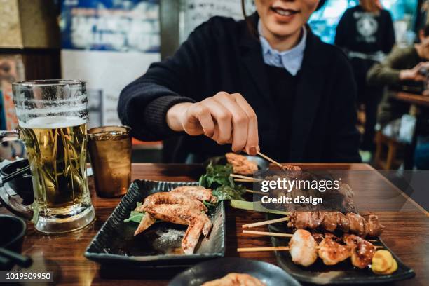 cropped image of woman enjoying traditional japanese yakitori and drinking beer in a japanese style restaurant - bier dunkel stock-fotos und bilder