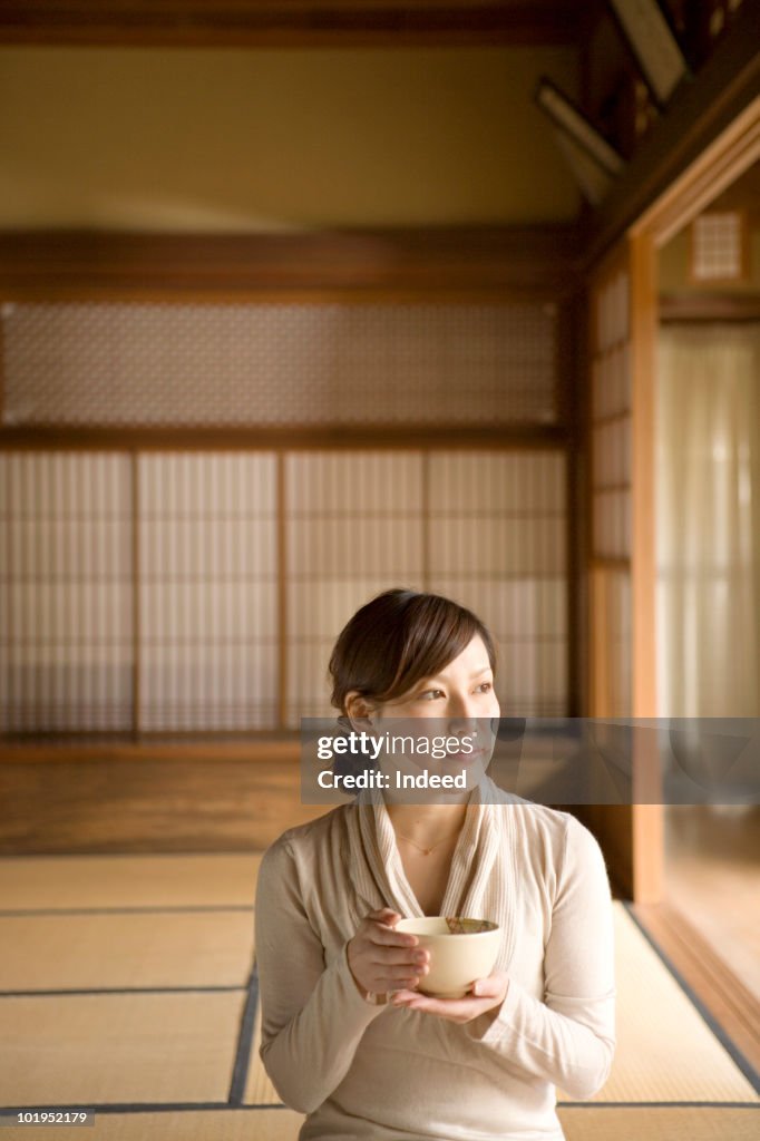 Young woman holding tea bowl, looking away