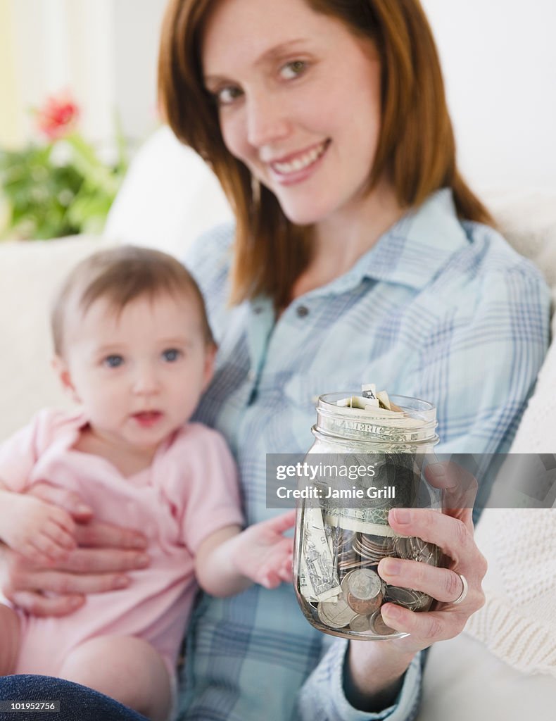 Mother holding baby and jar of money