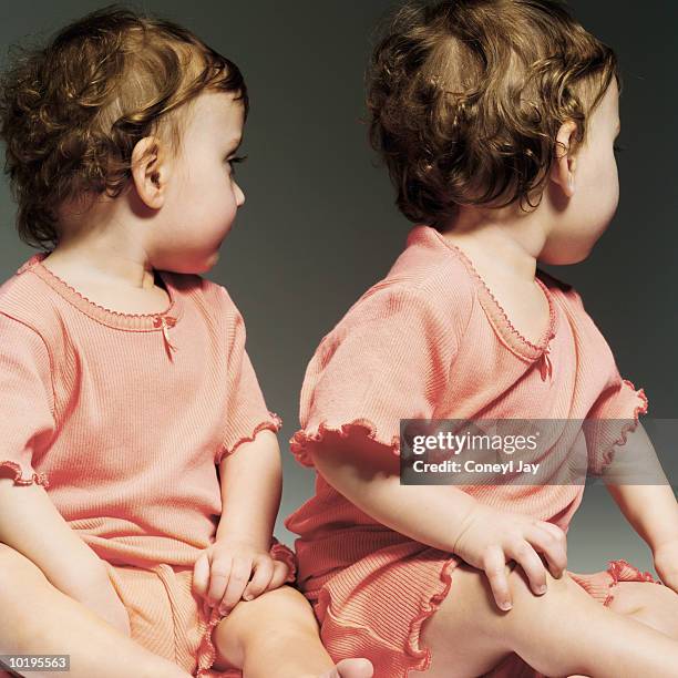 twin baby girls (9-12 months) in matching outfits, looking over should - identical twin stock pictures, royalty-free photos & images