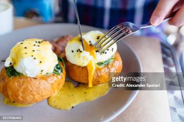 close up of eggs benedict with liquid egg yolk running out - gepocheerd stockfoto's en -beelden