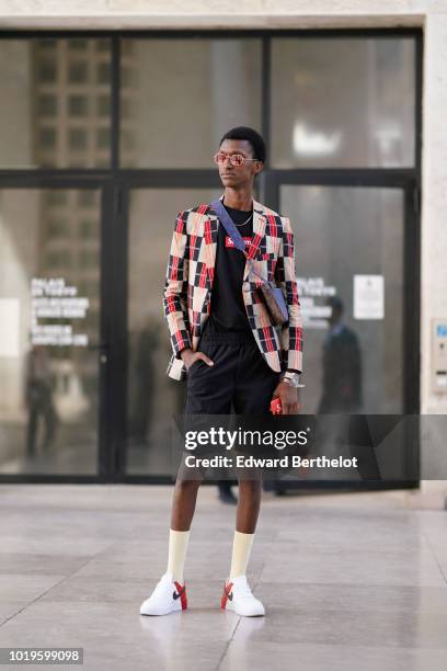 Model wears sunglasses, a black and red checked pattern blazer jacket, a black t-shirt from Supreme, black shorts, socks, Nike sneakers, outside Juun...