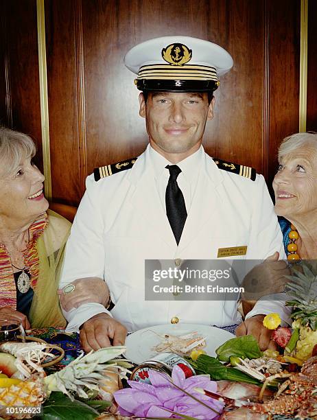 two mature women arm in arm with captain at table, smiling, portrait - boat captain stock pictures, royalty-free photos & images