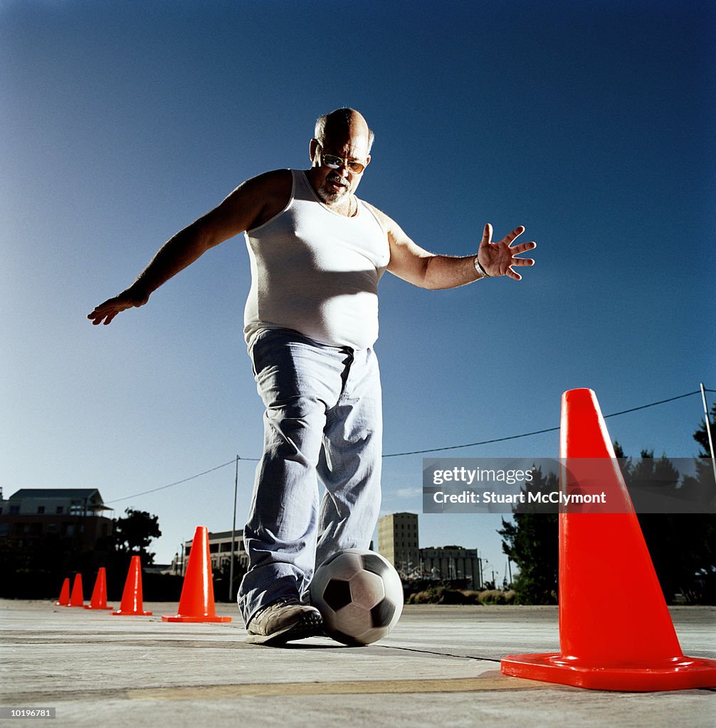 Mature man dribbling ball through cones