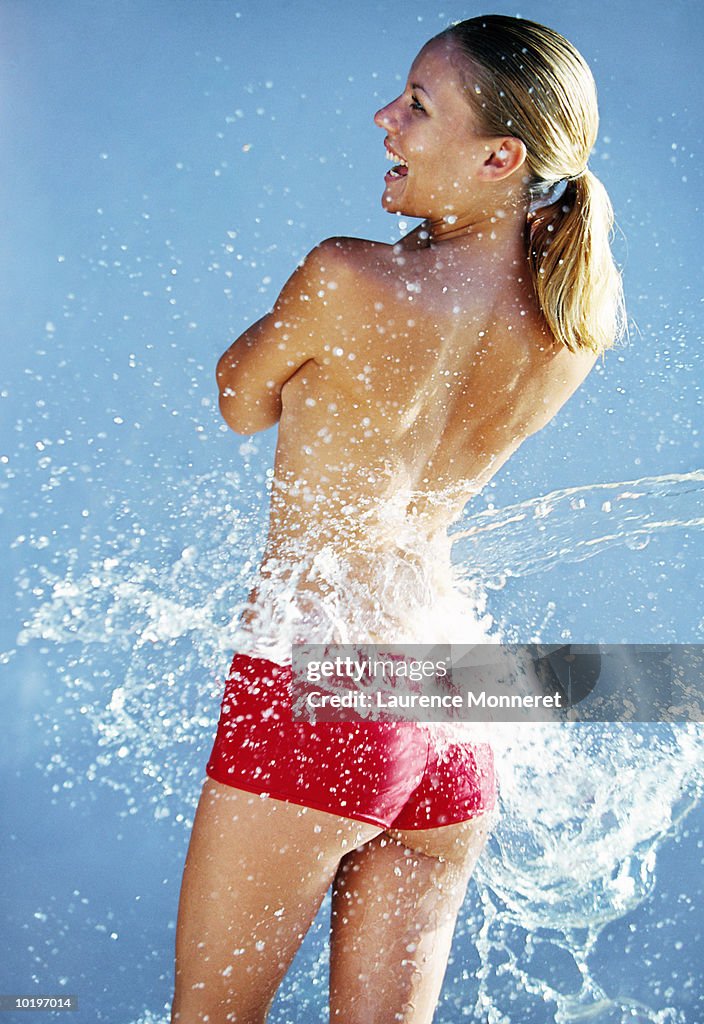 Young woman standing in water spray, rear view
