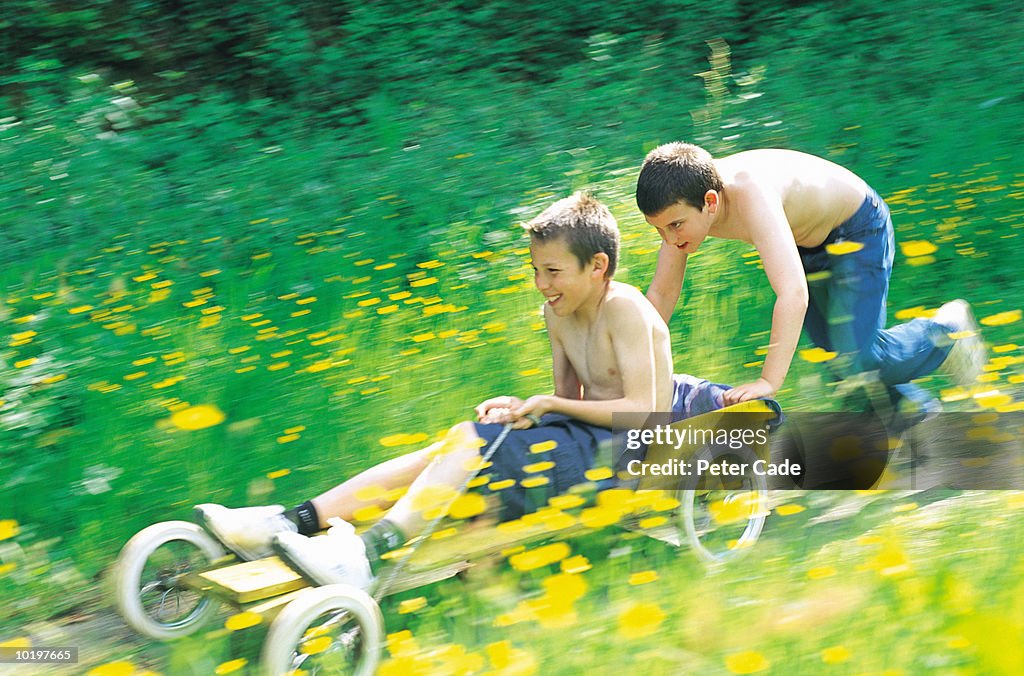 Two boys (10-12) playing with go-cart in field (blurred motion)