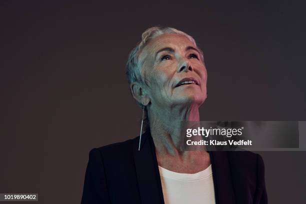 portrait of cool mature woman looking up, with coloured lights - aufschauen stock-fotos und bilder