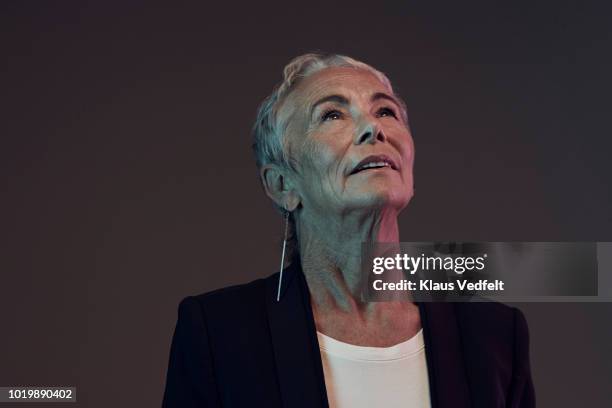 portrait of cool mature woman looking up, with coloured lights - business woman looking up stock pictures, royalty-free photos & images