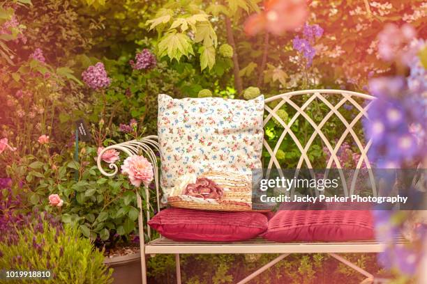 a beautiful summer cast iron garden chair with cushions and a summer hat, shabby chic scene - cast iron bench fotografías e imágenes de stock