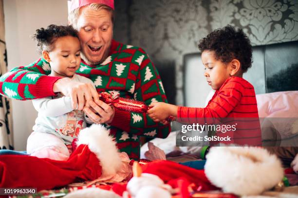 siblings pulling a christmas cracker with their father at christmas time - christmas cracker stock pictures, royalty-free photos & images