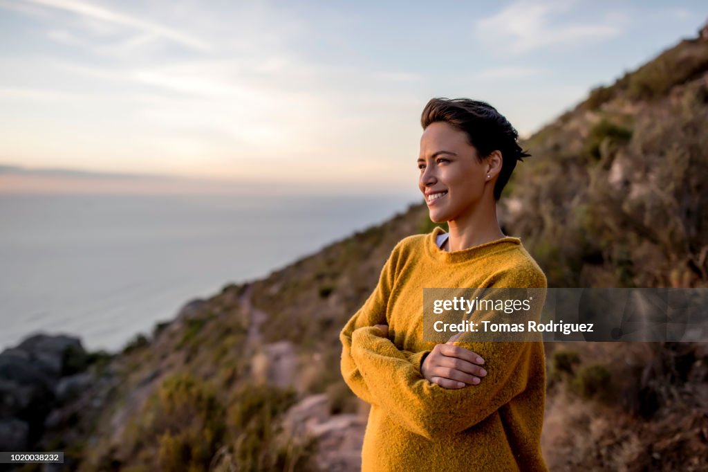 Smiling woman taking a break on a hiking trip looking at view at sunset