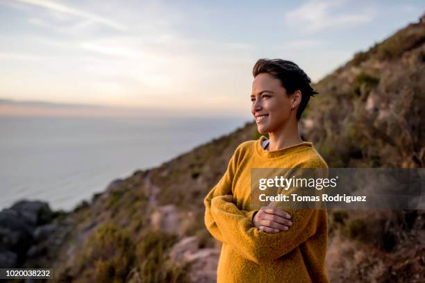 smiling woman taking a break on a hiking trip looking at view at sunset - mid adult woman sweater stock pictures, royalty-free photos & images
