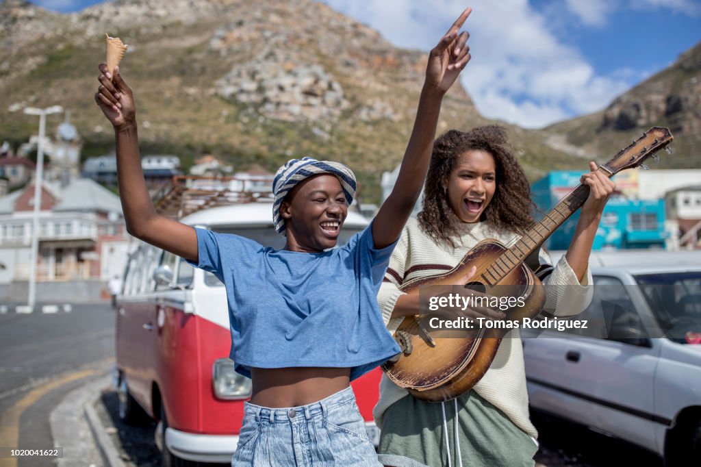 Two happy carefree female friends with guitar and ice cream cone at a van