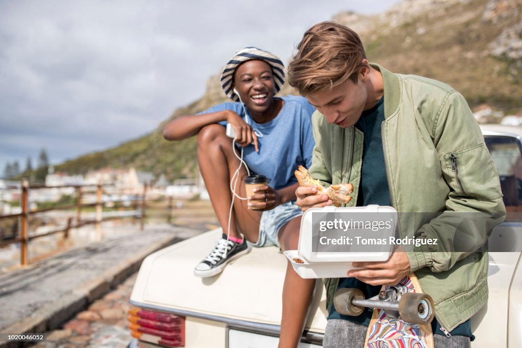 Happy young couple having a snack at a car