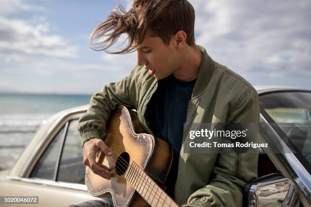 young man playing guitar at a car at the coast - car passion stock pictures, royalty-free photos & images