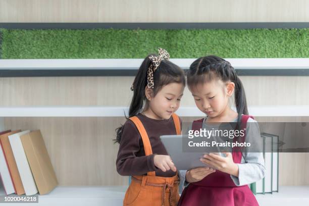 happy asian preschool students at school and playing with pc tablet together in classroom. education and technology concept. - pc 授業 ストックフォトと画像
