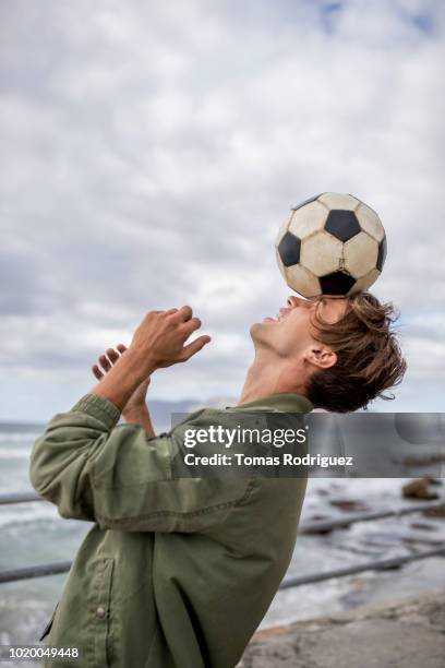 young man balancing soccer ball on his head at the coast - man playing ball fotografías e imágenes de stock