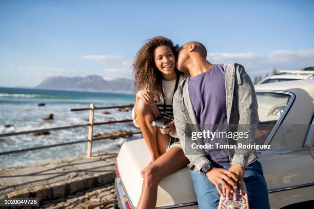 young man kissing girlfriend at a car at the coast - auto küssen stock-fotos und bilder