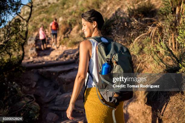 rear view of smiling woman with friends hiking on a mountain trail - hiking backpack stock pictures, royalty-free photos & images