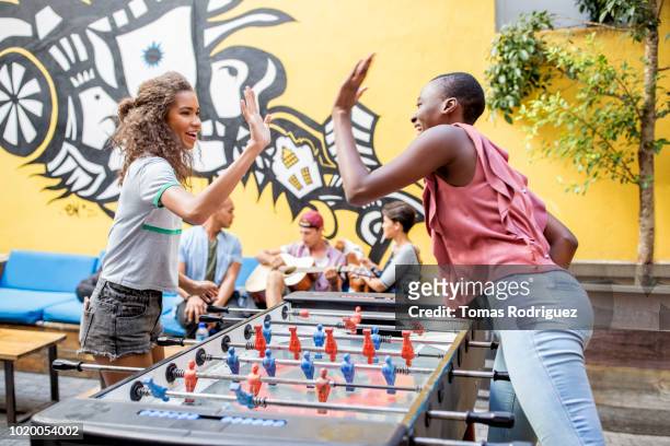 happy friends high fiving above foosball table in front of graffiti wall - black man high 5 stockfoto's en -beelden