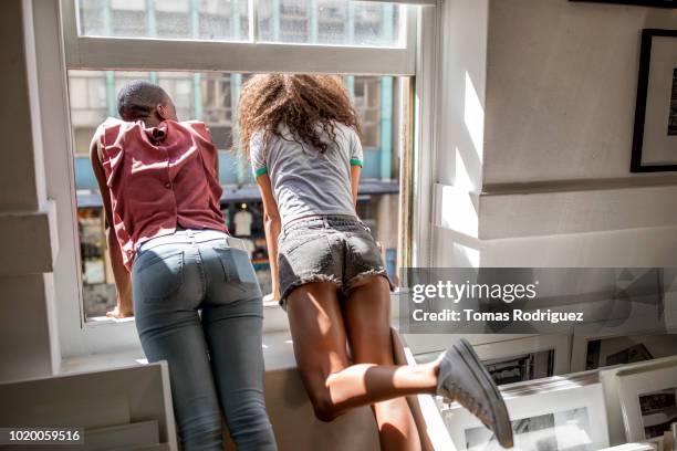 rear view of two young women leaning out of window - women in daisy dukes stock-fotos und bilder