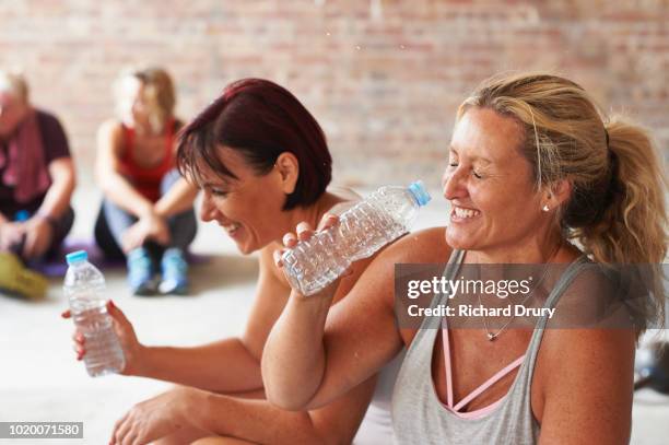 two women laughing and drinking from water bottles in the gym - women gym stock-fotos und bilder