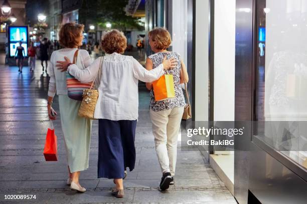 female senior friends shopping  in the city at night - woman looking over shoulder stock pictures, royalty-free photos & images