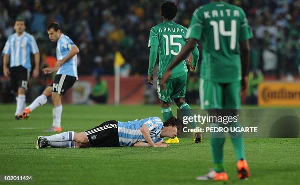 Argentina's striker Lionel Messi lies on teh pitch as Nigeria's midfielder Lukman Haruna and Nigeria's midfielder Sani Kaita walk by during Argentina...