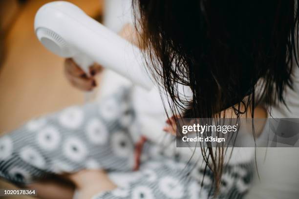 woman sitting on bed blow drying hair at home - blow drying hair stock pictures, royalty-free photos & images