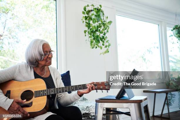 senior woman playing guitar at home - learn guitar stockfoto's en -beelden