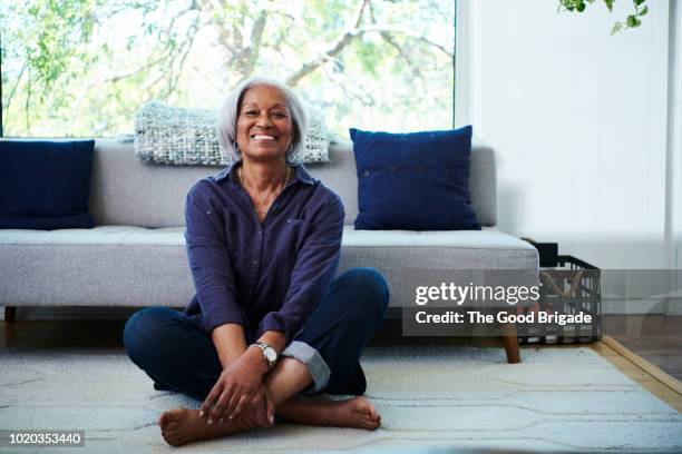 portrait of senior woman sitting on floor at home - assis en tailleur photos et images de collection