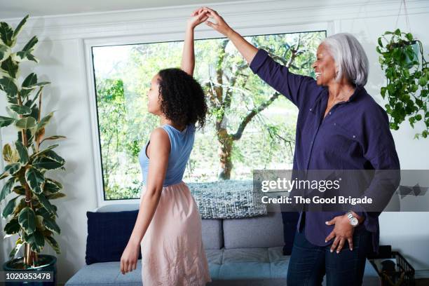 grandmother and granddaughter dancing in living room at home - grandmas living room stockfoto's en -beelden