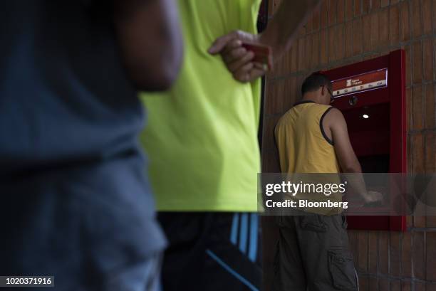 People wait in line to withdraw new sovereign bolivar banknotes at a Banco del Tesoro automated teller machine in Caracas, Venezuela, on Monday, Aug....