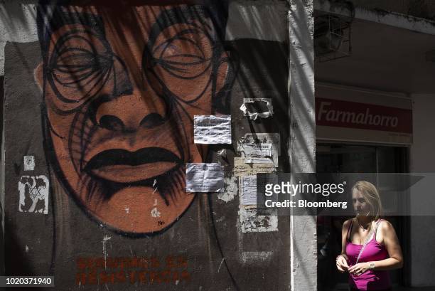 Woman walks past a pharmacy and graffiti that reads "We Continue In Resistance," in Caracas, Venezuela, on Monday, Aug. 20, 2018. The Venezuelan...