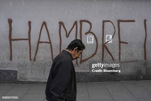 Man walks past graffiti that reads "Hunger" in Caracas, Venezuela, on Monday, Aug. 20, 2018. The Venezuelan government is re-denominating the bolivar...