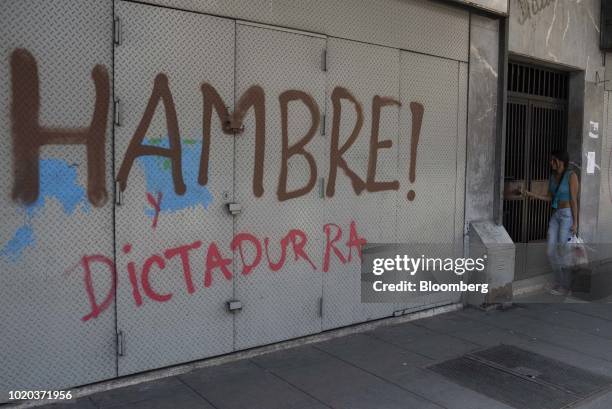 Woman enters a building with graffiti that reads "Hunger And Dictatorship," in Caracas, Venezuela, on Monday, Aug. 20, 2018. The Venezuelan...