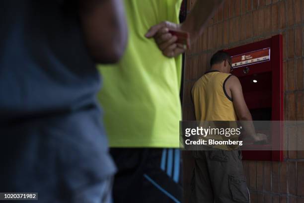 People wait in line to withdraw new sovereign bolivar banknotes at a Banco del Tesoro automated teller machine in Caracas, Venezuela, on Monday, Aug....
