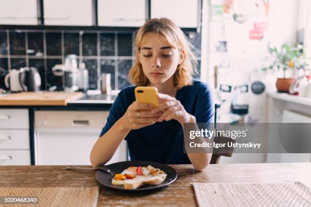 young woman using smartphone at breakfast - ausdruckslos stock-fotos und bilder