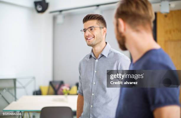 lächelnde junge unternehmer im gespräch mit kollegen im büro - cool modern mann büro business stock-fotos und bilder