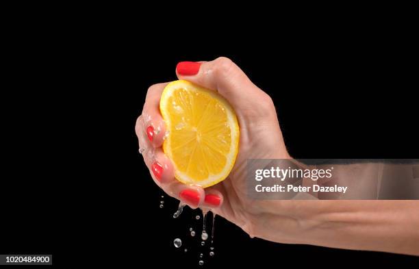 woman squeezing a lemon against black background - spremere foto e immagini stock