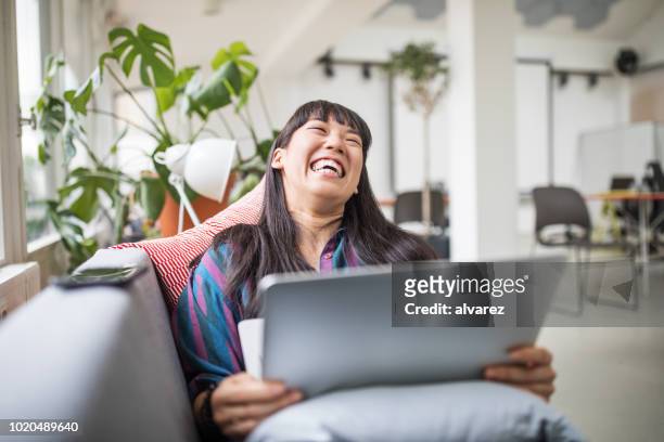 businesswoman lying on sofa with laptop in modern office lounge - cool attitude stock pictures, royalty-free photos & images