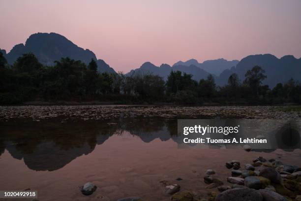 silhouette of a karst limestone mountains and their reflections on the nam song river in vang vieng, vientiane province, laos, at sunset. - shallow 2018 song stock-fotos und bilder