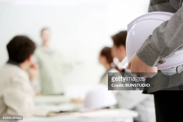 engineer holding hard hat in meeting - lavoro e impiego foto e immagini stock