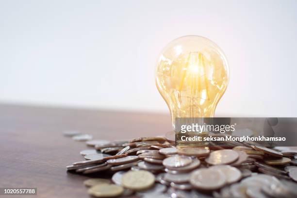 light bulb and pile of coins with copy space - saving electricity stock pictures, royalty-free photos & images