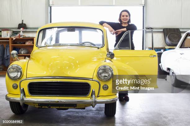a caucasian female stands next to her old car in a classic car repair shop. - old car stock-fotos und bilder