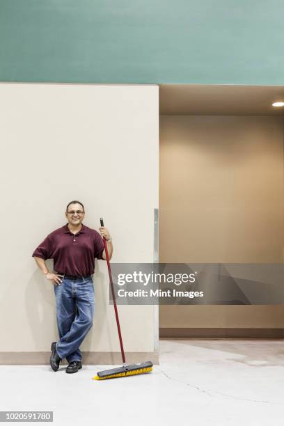 an hispanic workman standing in a large interior space with a broom. - hauswart stock-fotos und bilder