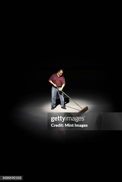 a man with a broom working in an area of a floor lit up by a spotlight. - spot lit photos et images de collection