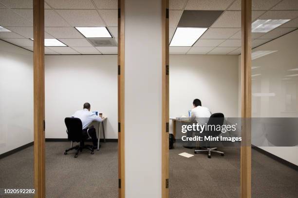 a view of two businessmen working on opposite sides of a wall in two different office spaces. - loneliness work stock pictures, royalty-free photos & images