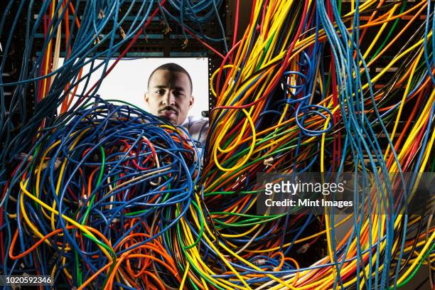 a black male technician working on a tangled mess of cat 5 cables in a server room. - cable mess stockfoto's en -beelden