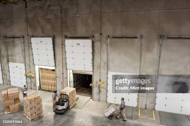 a team of three mixed race uniformed warehouse workers loading boxed products into the back of a truck in a distribution warehouse. - loading dock 個照片及圖片檔